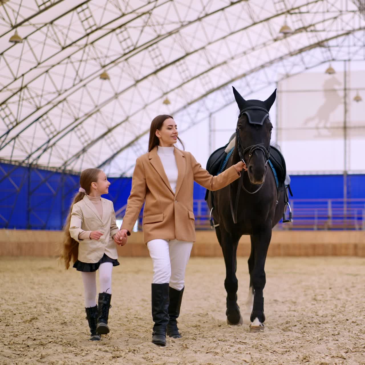 Woman and young girl leading a gorgeous black horse. Mother and daughter spending time at riding hall. Horse riding hobby concept
