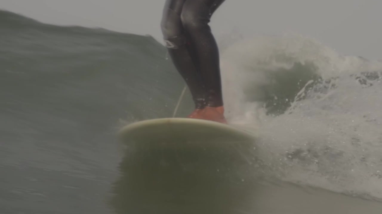 Primo piano di un surfista di longboard irriconoscibile che cavalca un'onda e schizza acqua sulla telecamera