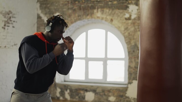 Pugile afroamericano che pratica shadowboxing con le cuffie in una sala luminosa.