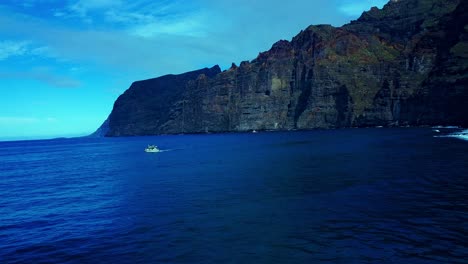 Bote-Pequeño-Navegando-En-Un-Océano-Azul-Abierto-Frente-A-Montañas-Rocosas-De-Gran-Altura,-España