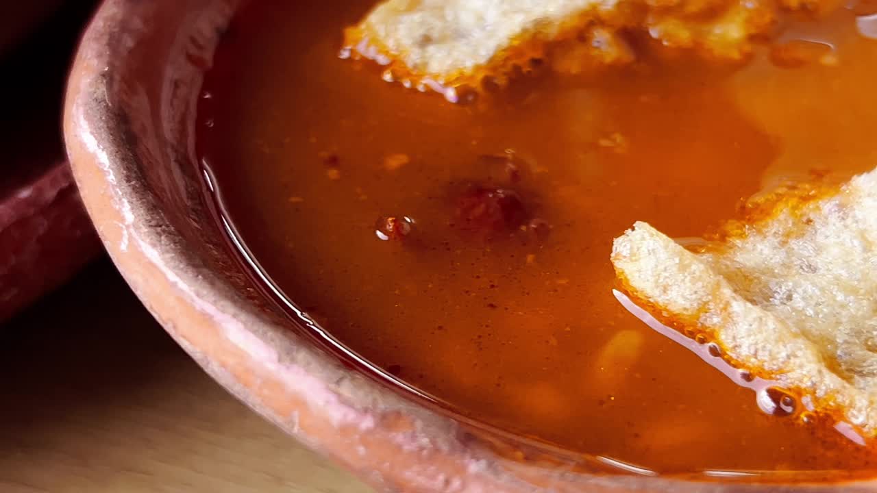 Crispy bread piece loating in Spicy Broth or sauce as condiment for mexican pozole, the vibrant orange color and texture highlight the dish's savory and flavorful nature, perfect for a hearty meal