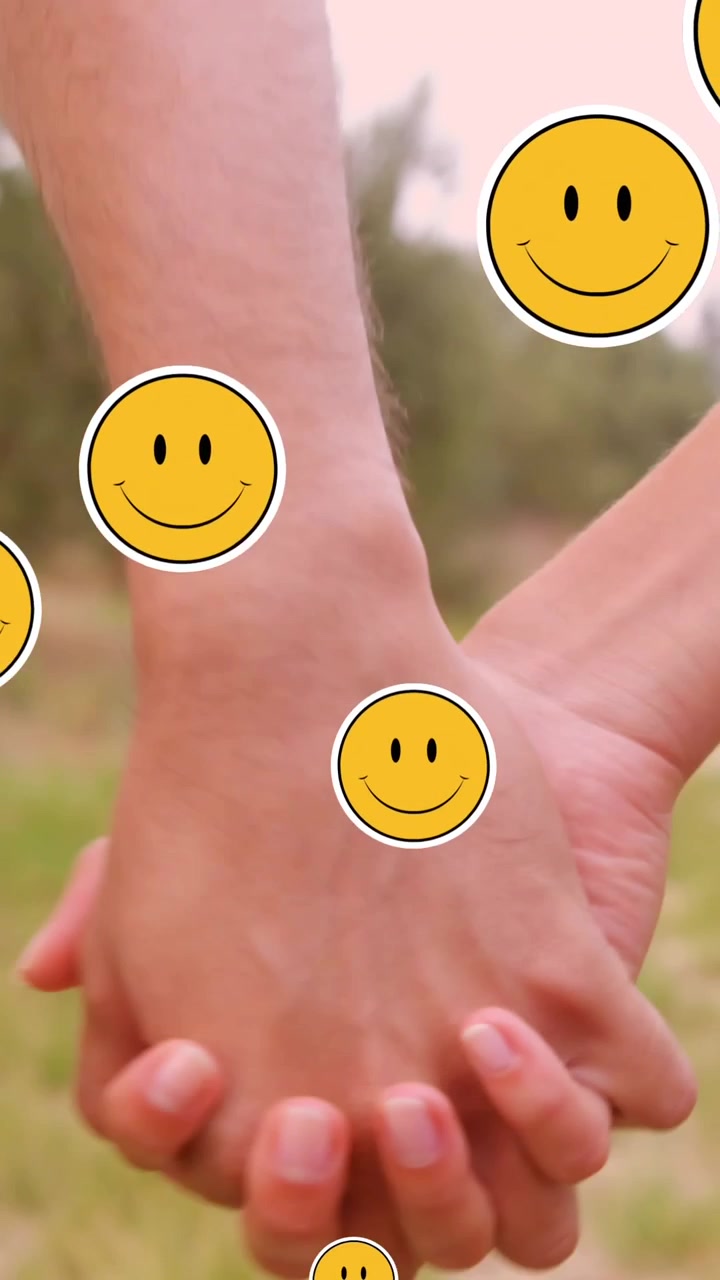 Multiple smiling face emoji floating against mid section of couple holding hands
