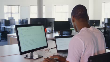 rear view of young black male executive working desktop pc and laptop in modern office 4k