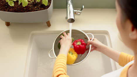 washing bell peppers in colander under running water in kitchen sink