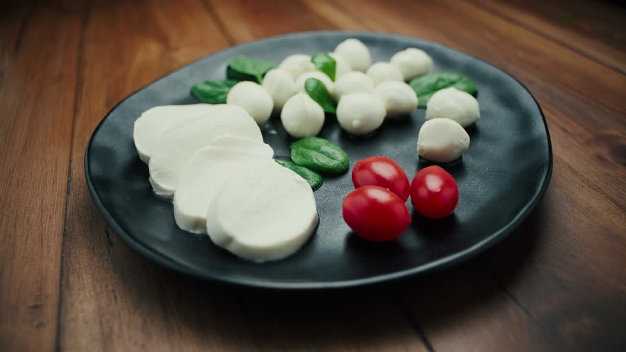 pequeñas bolas de queso mozzarella blanco, hojas de espinaca y tomates en un plato negro.