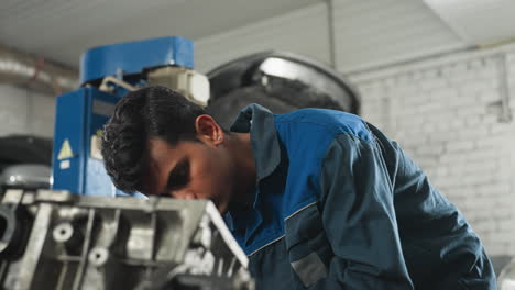 engineer in mechanical workshop concentrating on car engine repair while colleague observes closely, background features industrial tools, machinery, and open car hood