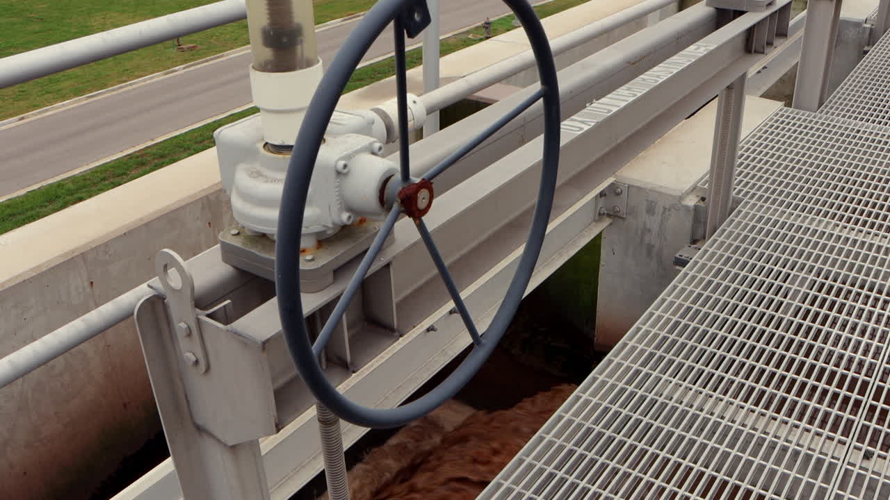 A valve at a wastewater treatment plant’s anaerobic basin releases flowing brown sewage water, showcasing the controlled movement within the treatment process
