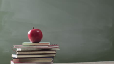 video of books and apple on wooden table over mathematical formulas on blackboard