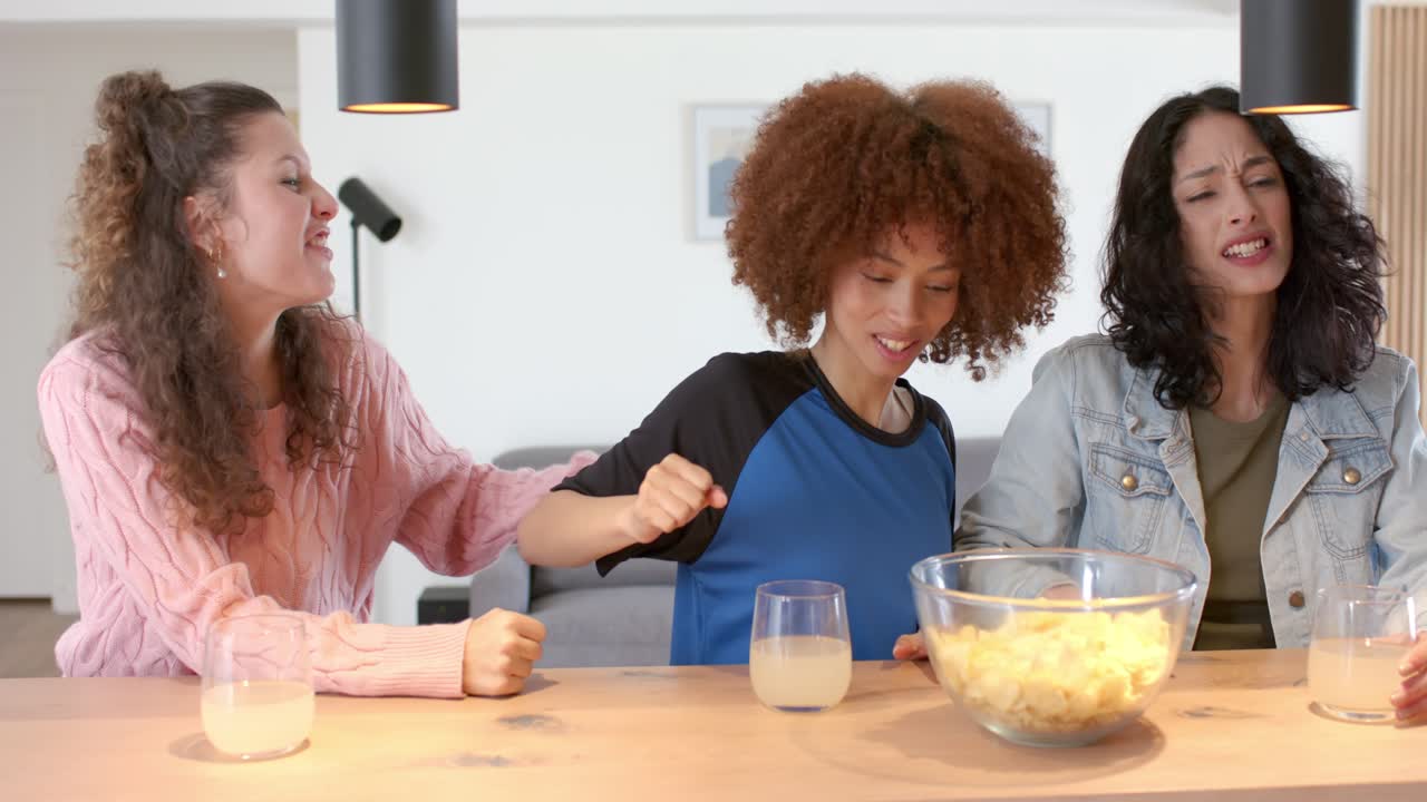 Många kvinnliga vänner som reagerar på en händelse utanför bild, tar chips, går armkrok, skrattar vid bordet