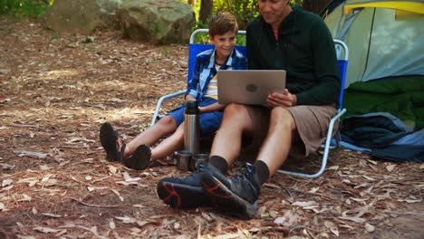 father and son using laptop outside tent