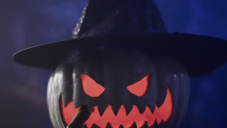 Video-of-halloween-carved-pumpkin-with-hat-and-smoke-with-copy-space-on-blue-background