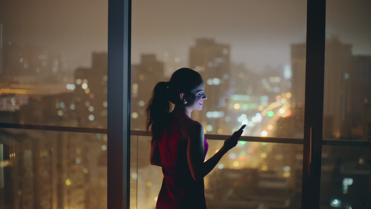 noche mujer riendo teléfono móvil en la ventana panorámica. dama esperando por la noche