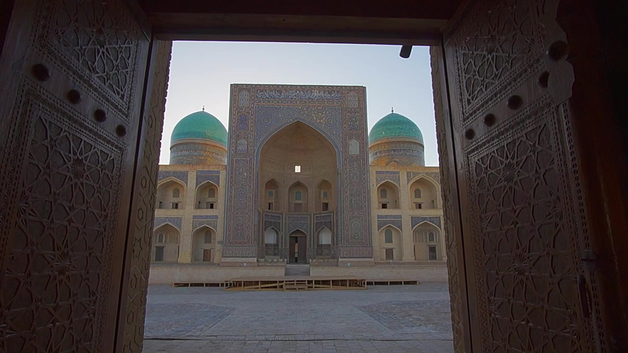 Una vista de una gran madrasa desde detrás de una gran puerta en Bujará, Uzbekistán