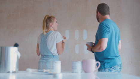 couple renovating kitchen at home painting tester paint colour strips on wall