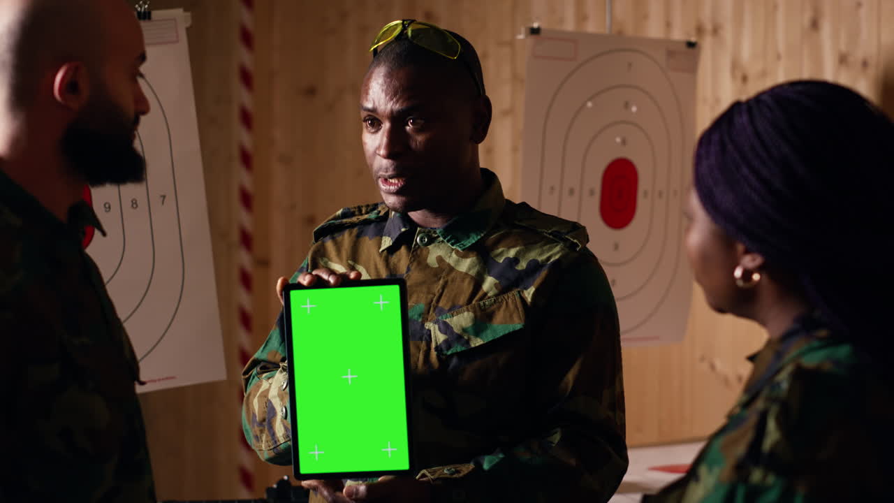Soldiers watching instructional videos on green screen tablet shown by commander