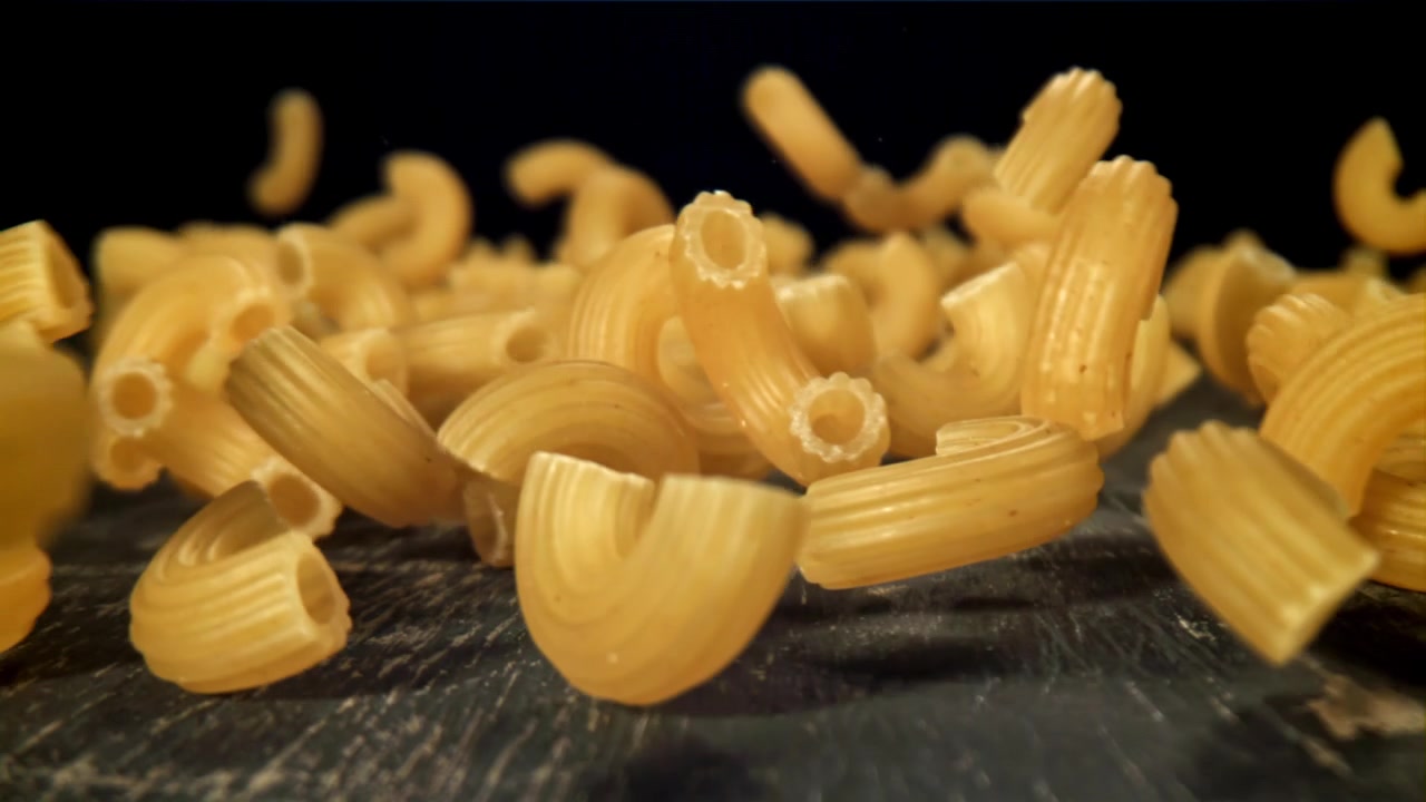 Pasta di maccheroni secchi che cadono al rallentatore su una superficie scura