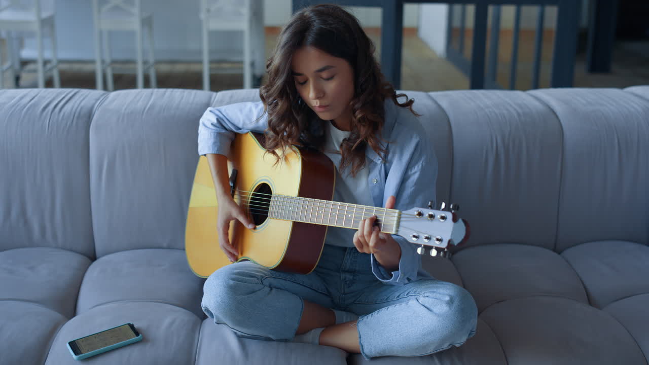 niña enfocada aprendiendo a tocar la guitarra en casa. mujer joven tocando la guitarra
