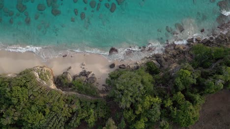 Aerial-top-down-shot-of-beautiful-sandy-beach-with-clear-sea-water-and-green-cliff-mountains---Playa-Chencho,-Dominican-Republic