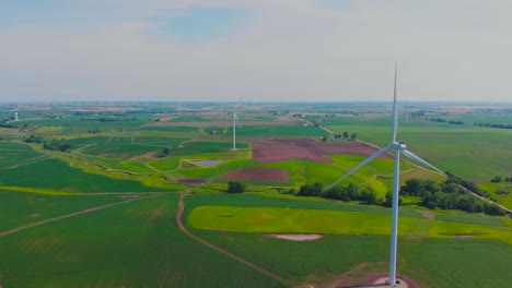 Colorful-green-hues-beneath-rotating-wind-turbines-in-rural-countryside-field-on-sunny-day,-backward-aerial