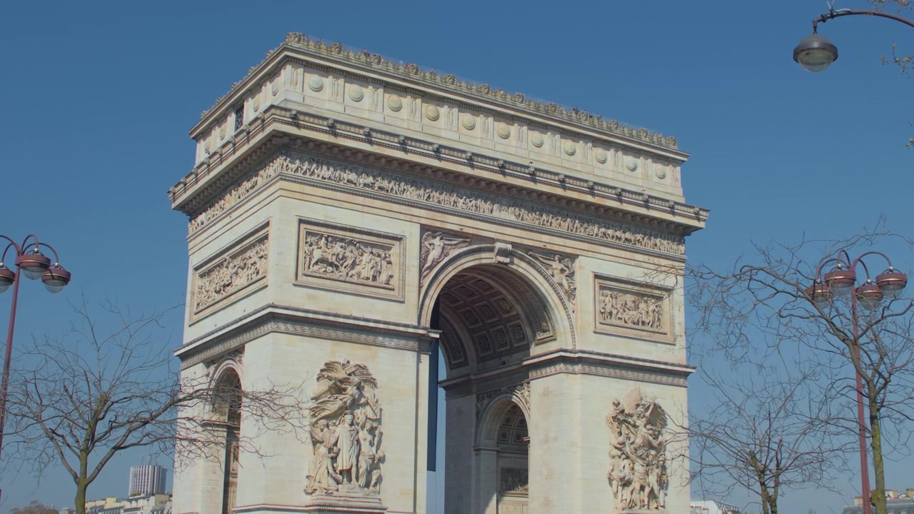 Nærbillede af arkitektonisk detalje på Triumfbuen i Paris, håndholdt optagelse. Historisk fransk vartegn med facade af udskårne stenrelieffer under en blå himmelbaggrund.