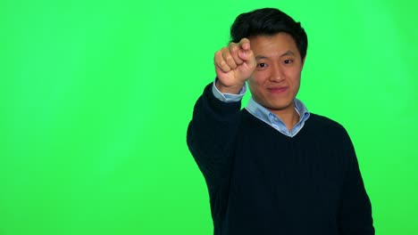 a young asian man points at the camera with a smile - green screen studio