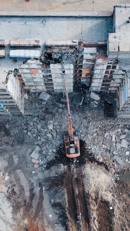 a demolition excavator destroys an old unusable building. destruction of walls and concrete blocks. aerial view. vertical video