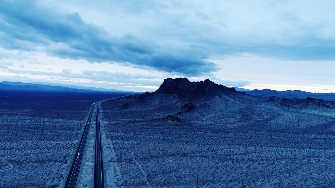 Empty desert road winds through rocky terrain as sky glows before sunrise