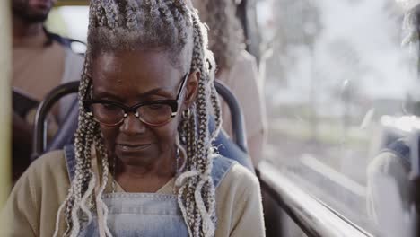 Elderly Black Woman with Braids and Glasses Riding a Bus
