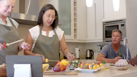 in kitchen, senior diverse women preparing vegetable skewers together, focusing on cooking, at home