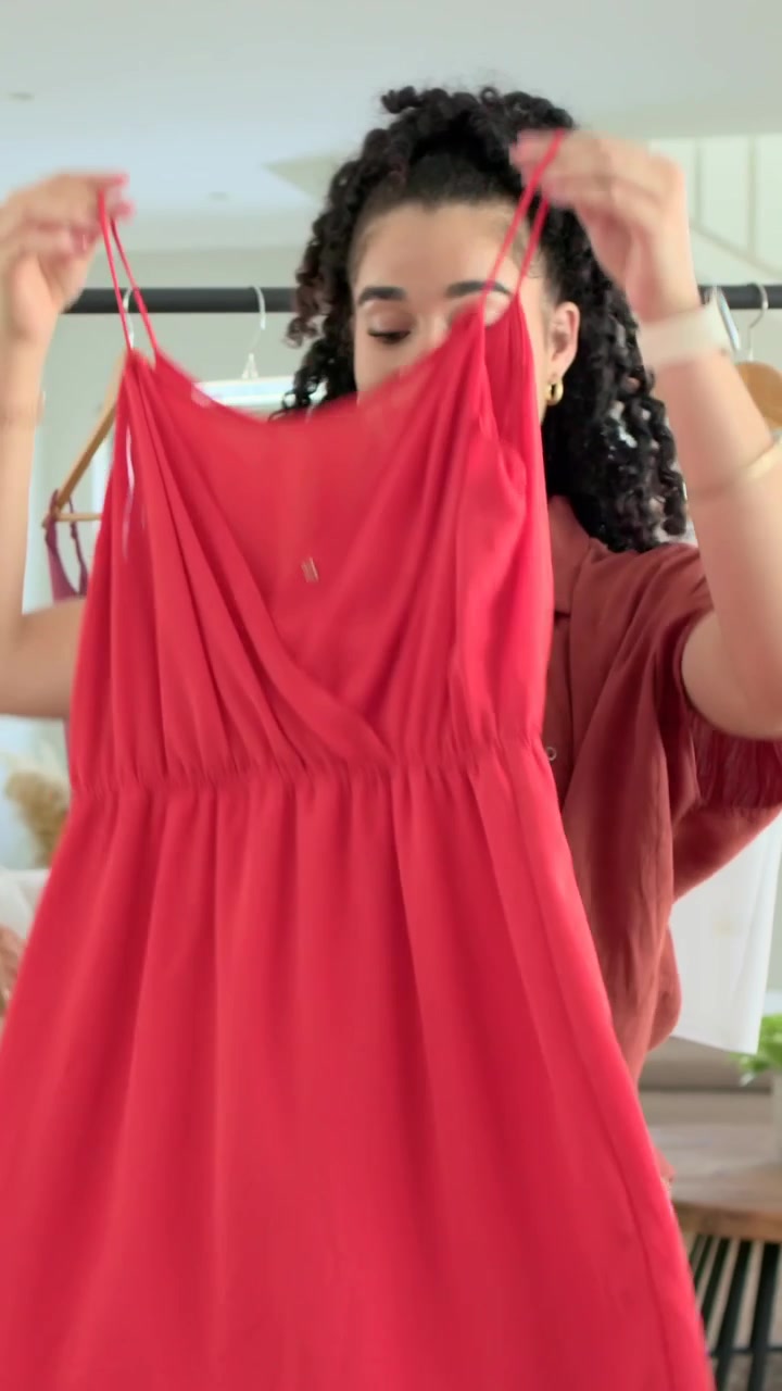 Video verticale: donna con top color ruggine che guarda il laptop a casa, prende un vestito rosso dall'appendiabiti e ne controlla la vestibilità.