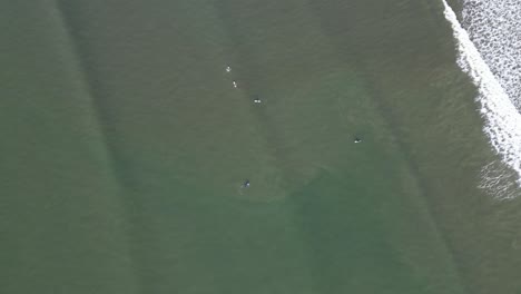 Aerial-view-of-surfers-in-ocean-waves,-casting-long-shadows-in-the-morning-light-at-Lahinch-beach