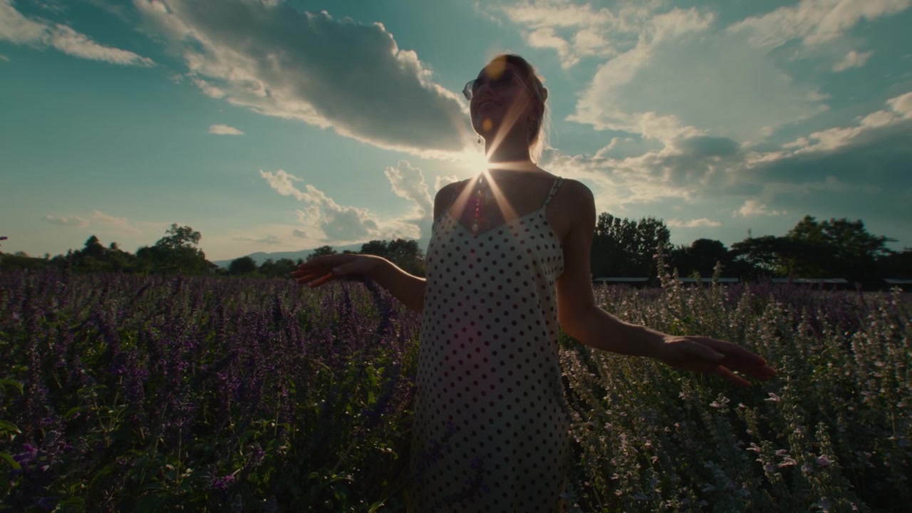 Giovane donna in piedi in un campo di fiori viola al tramonto