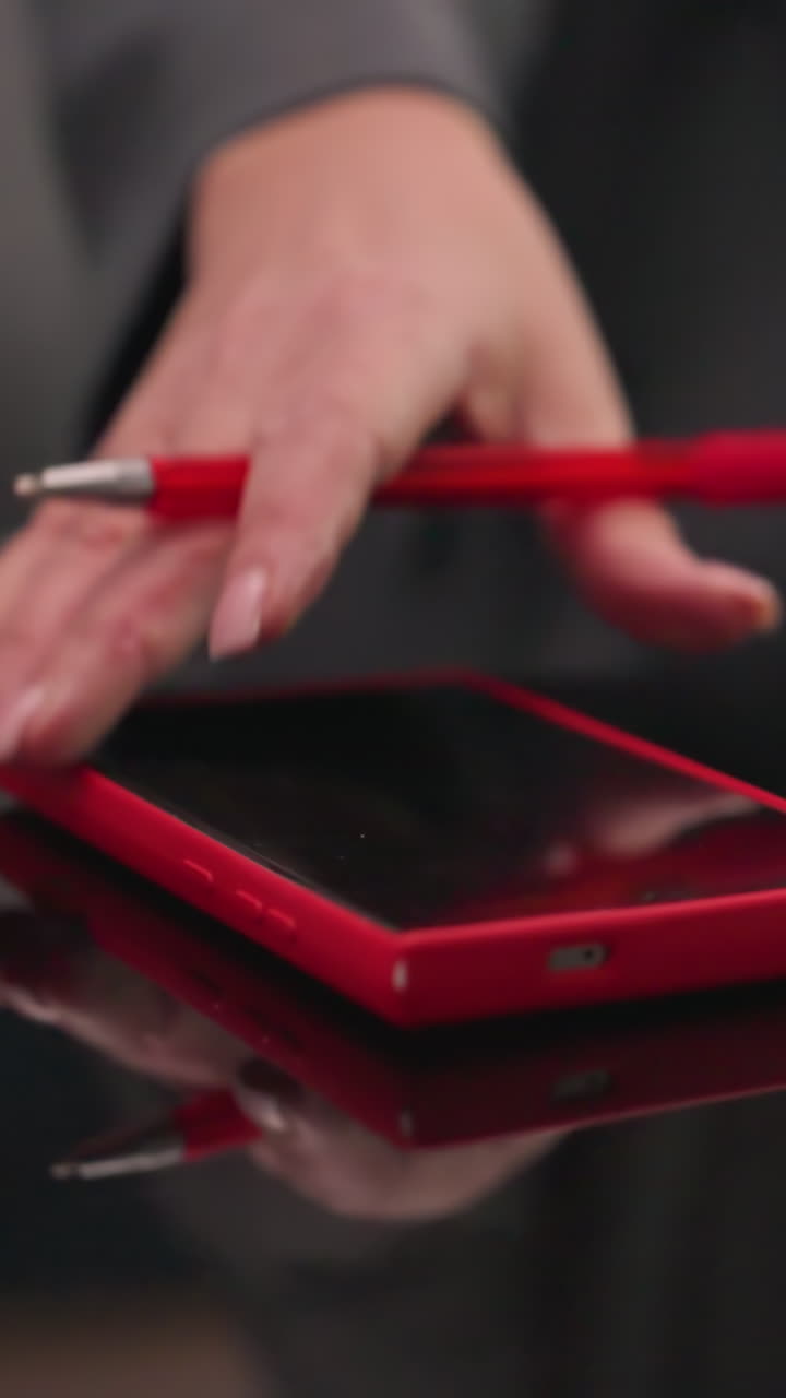 Close-up of red smartphone on top of red notebooks and laptop on glossy desk in office setting. Focus on work tools, productivity, and organized corporate workspace