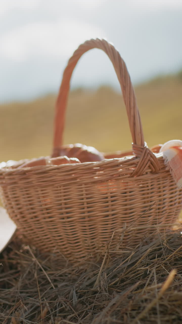 sombrero de sol y canasta de picnic tejida llena de bocadillos descansa en la bala de heno en vastas tierras de cultivo con el brillo cálido de la luz solar, el entorno rústico del campo evoca el tranquilo ocio al aire libre y el encantador estilo de vida rural
