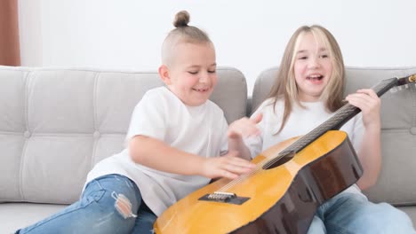 brother and sister have fun sitting on the couch, they play the guitar. happy children playing guitar