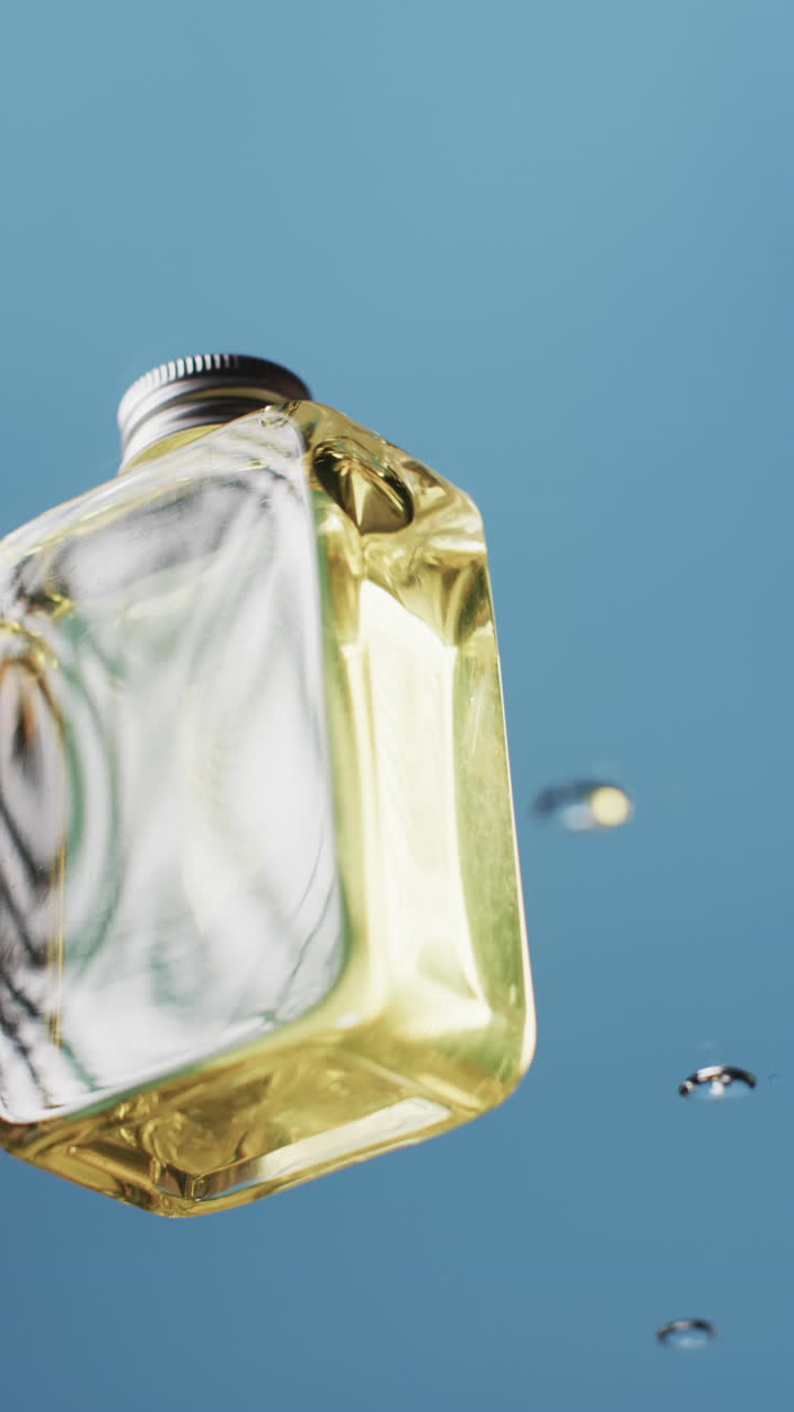 Vertical video of drops falling on beauty product bottle with copy space on blue background