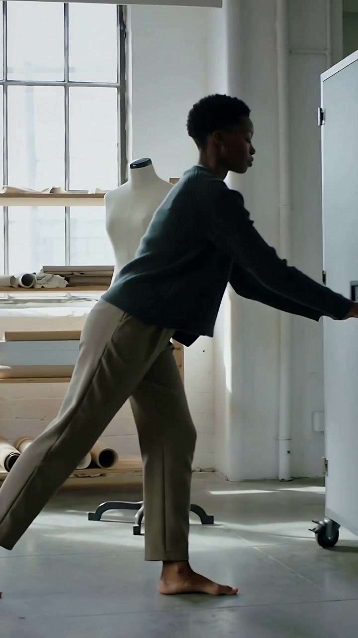 Vertical video: Raising arms barefoot-designer walking studio and opening cabinet reaching inside