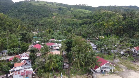 Filipino-villager-seaside-houses-and-coastline-road-traffic-at-lush-green-overgrown-foothill-on-Cebu-island