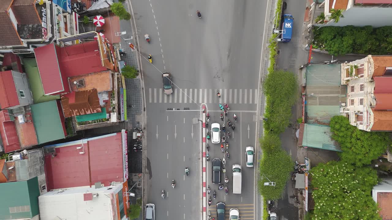Rising top-down drone shot of a bustling urban intersection in Hanoi, Vietnam. The dense network of streets and buildings with vehicles moving through the traffic. UHD