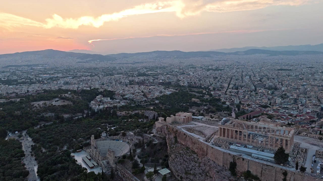 L'Acropoli di Atene e l'Odeon di Erode Attico si ergono su quartieri estesi sotto un caldo cielo al tramonto.