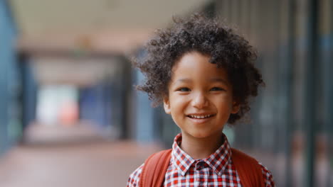 portrait of smiling male elementary school pupil outdoors with backpack at school