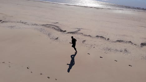 Aéreo,-Disparo-De-Un-Dron-Siguiendo-A-Un-Hombre-Corriendo-En-Una-Playa,-Día-Soleado,-En-La-Isla-Langeoog,-En-El-Nordsee,-En-El-Norte-De-Alemania