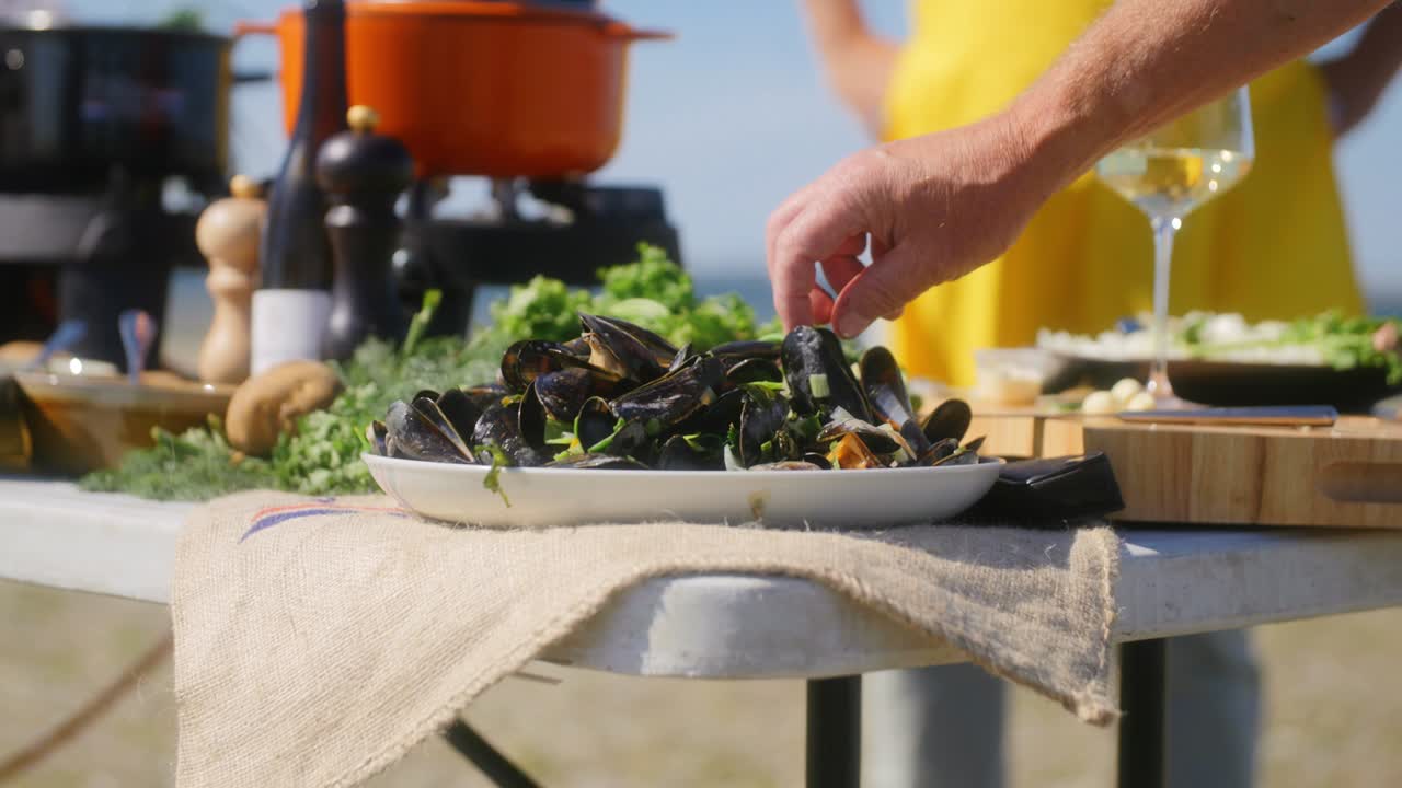A table with a plate full of mussels and a hand grabbing one mussel to open and eat in slowmotion