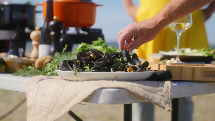 A table with a plate full of mussels and a hand grabbing one mussel to open and eat in slowmotion