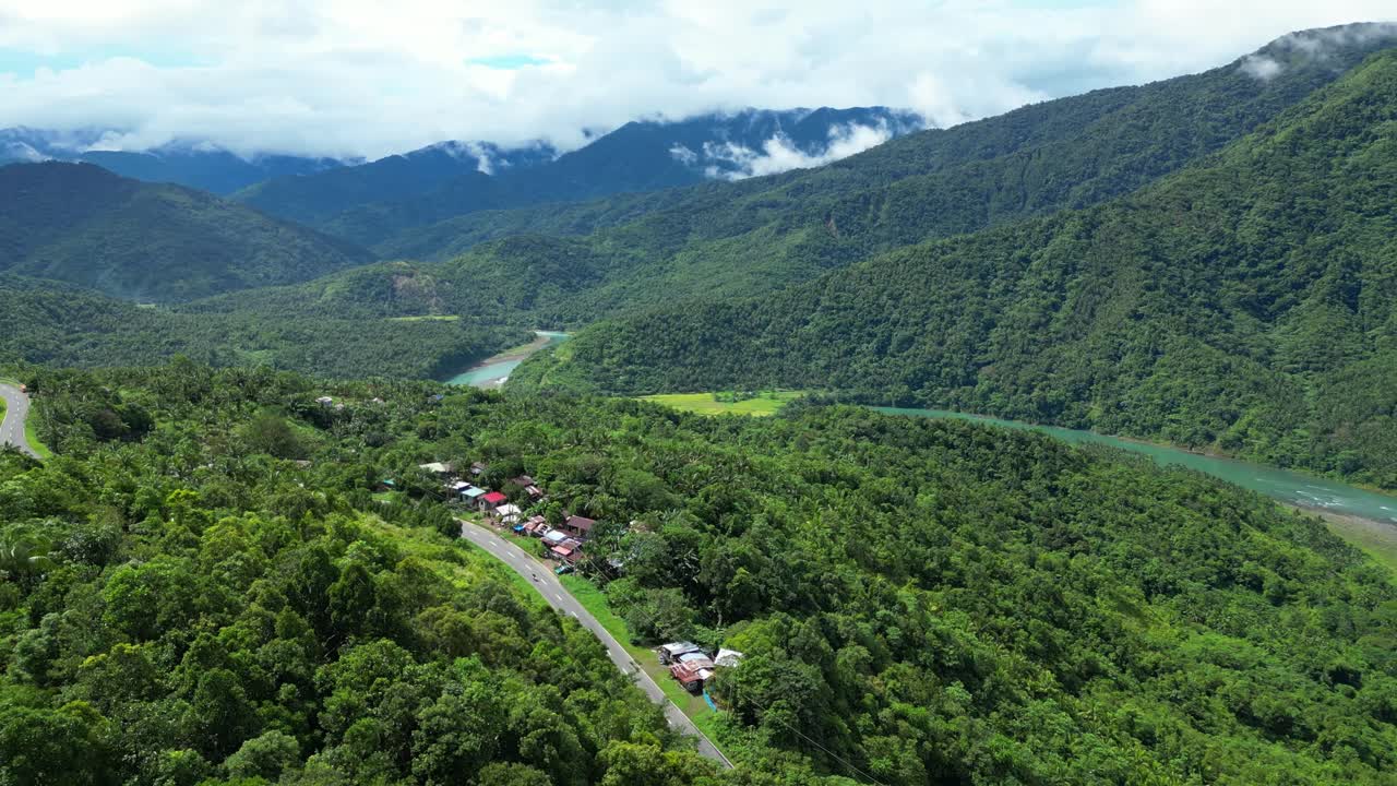 Ripresa aerea frontale di una vallata montana boscosa con fiume tortuoso, villaggio con tetti rossi e bianchi e cime coperte di nuvole a Tanay Rizal, Filippine