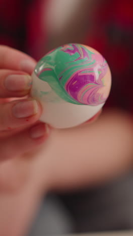 female artist turns vibrant easter egg with colorful patterns of marbling design at table closeup slow motion. idea for traditional holiday celebration