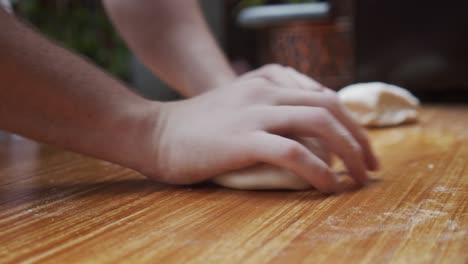 Chef-rounds-the-pizza-dough-parts-on-wooden-table