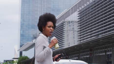 African-american-businesswoman-walking-with-smartphone-and-coffee-in-city