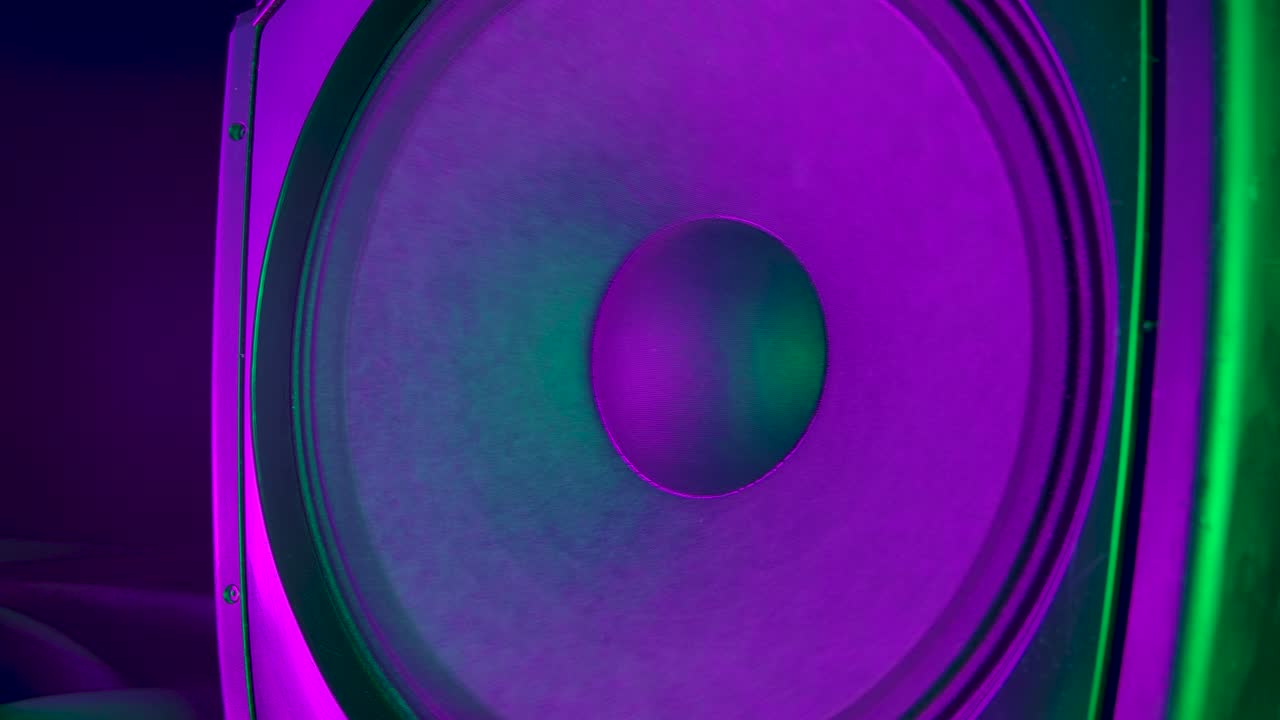 Membranas de alto-falantes de áudio tocando música moderna, produzindo som de subwoofer potente. Coloridas com luzes neon de discoteca vibrantes. Conceito de festa de rock ou dança. Close-up. Câmera lenta.