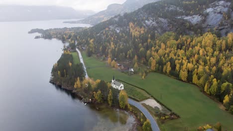 Small-Norwegian-church-in-a-autumn-colored-valley,-low-clouds,-fog-and-rain